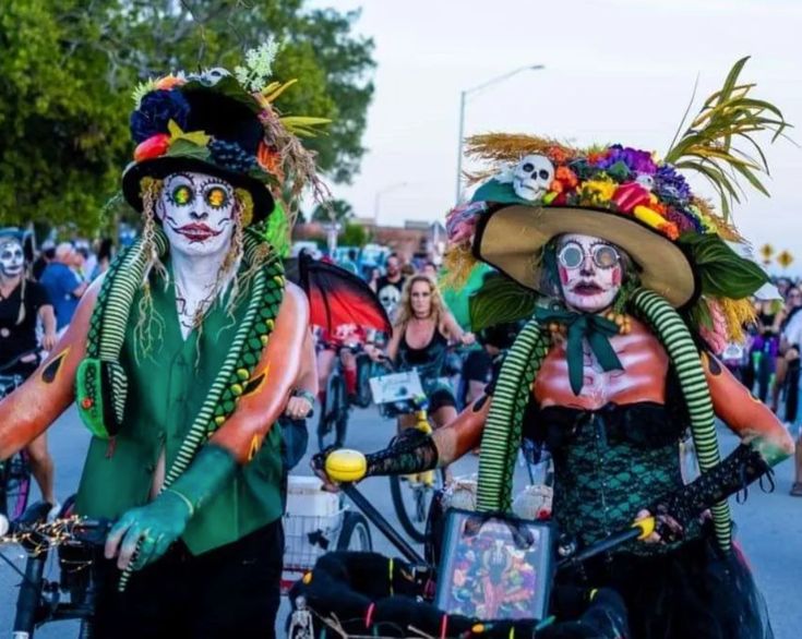 two clowns are riding their bikes down the street with people dressed up in costumes