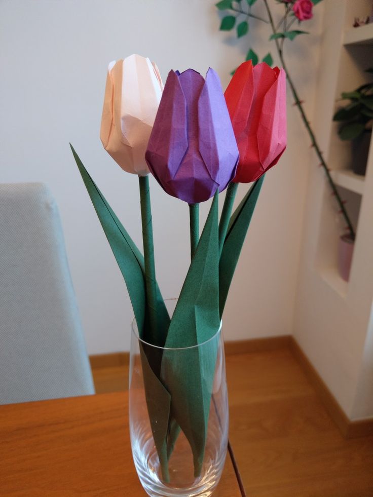 three origami tulips in a glass vase on a table with flowers