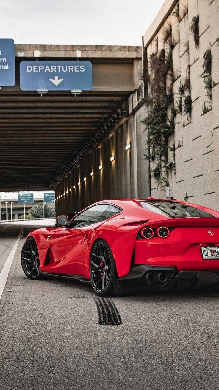 a red sports car is parked in front of an airport entrance sign and underpass