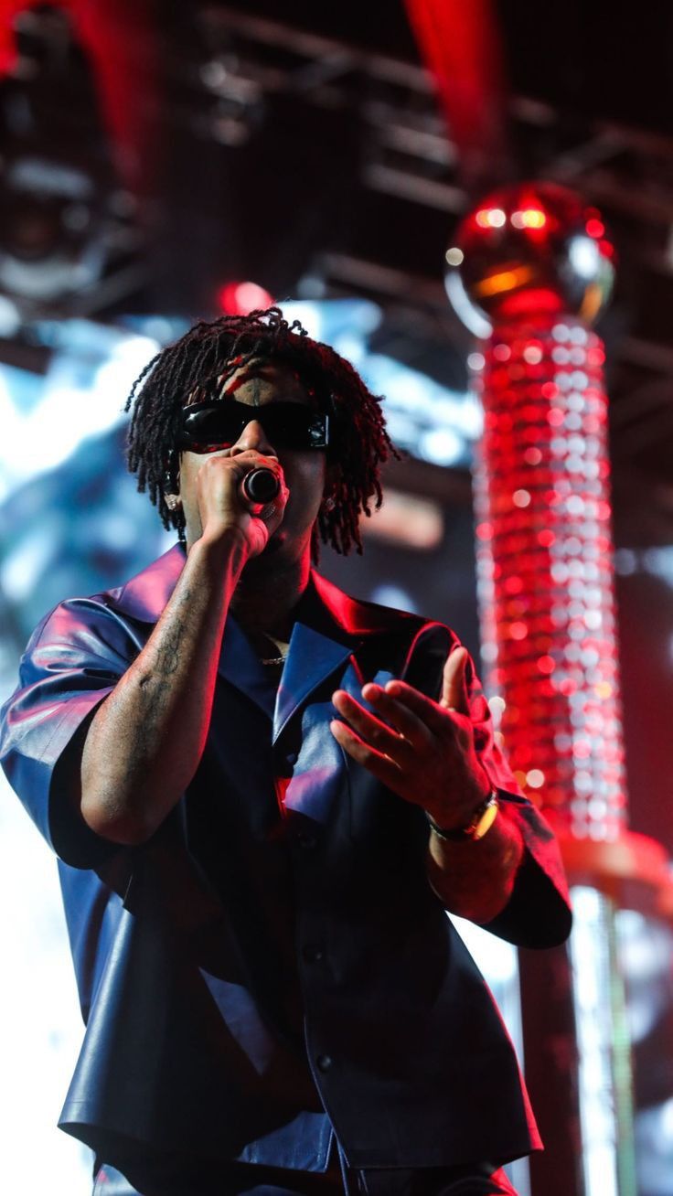 a man standing on top of a stage holding his hand up to his mouth while wearing sunglasses