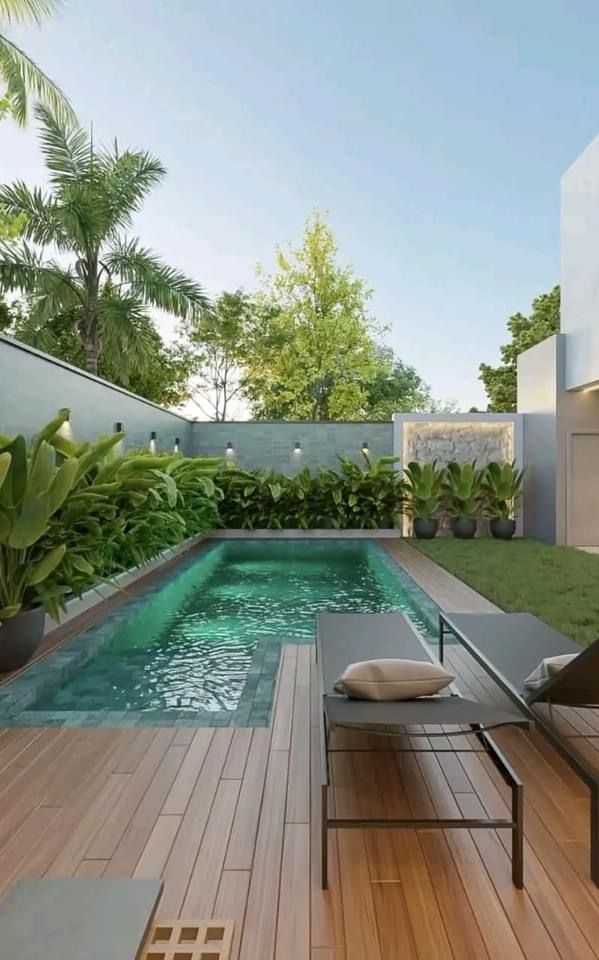 an outdoor swimming pool surrounded by greenery and wooden decking with lounge chairs around it