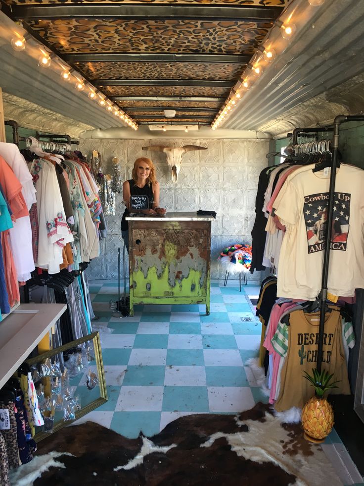 a woman standing behind a counter in a room with lots of clothes on display and lights hanging from the ceiling