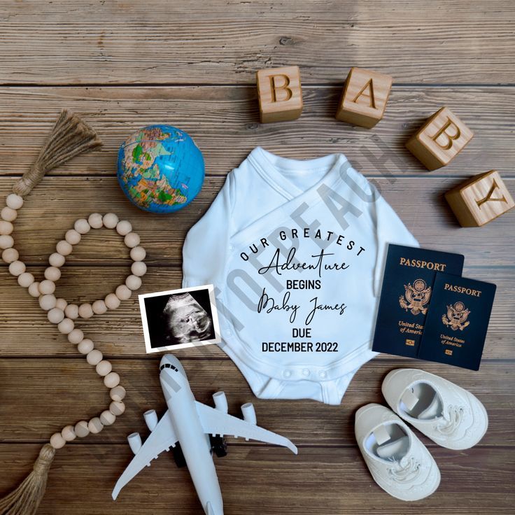 a baby's bodysuit, passport, and other items laid out on a wooden floor