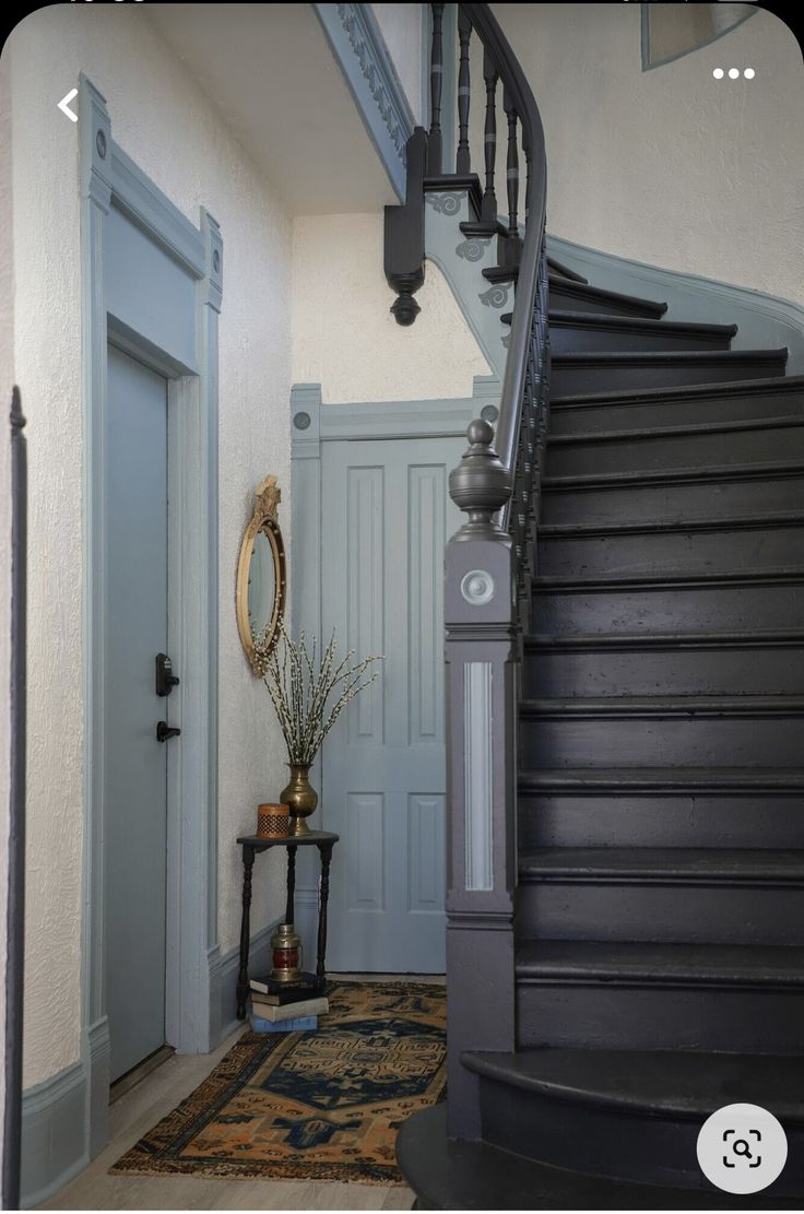 an entry way with stairs and a mirror on the wall next to a vase filled with flowers