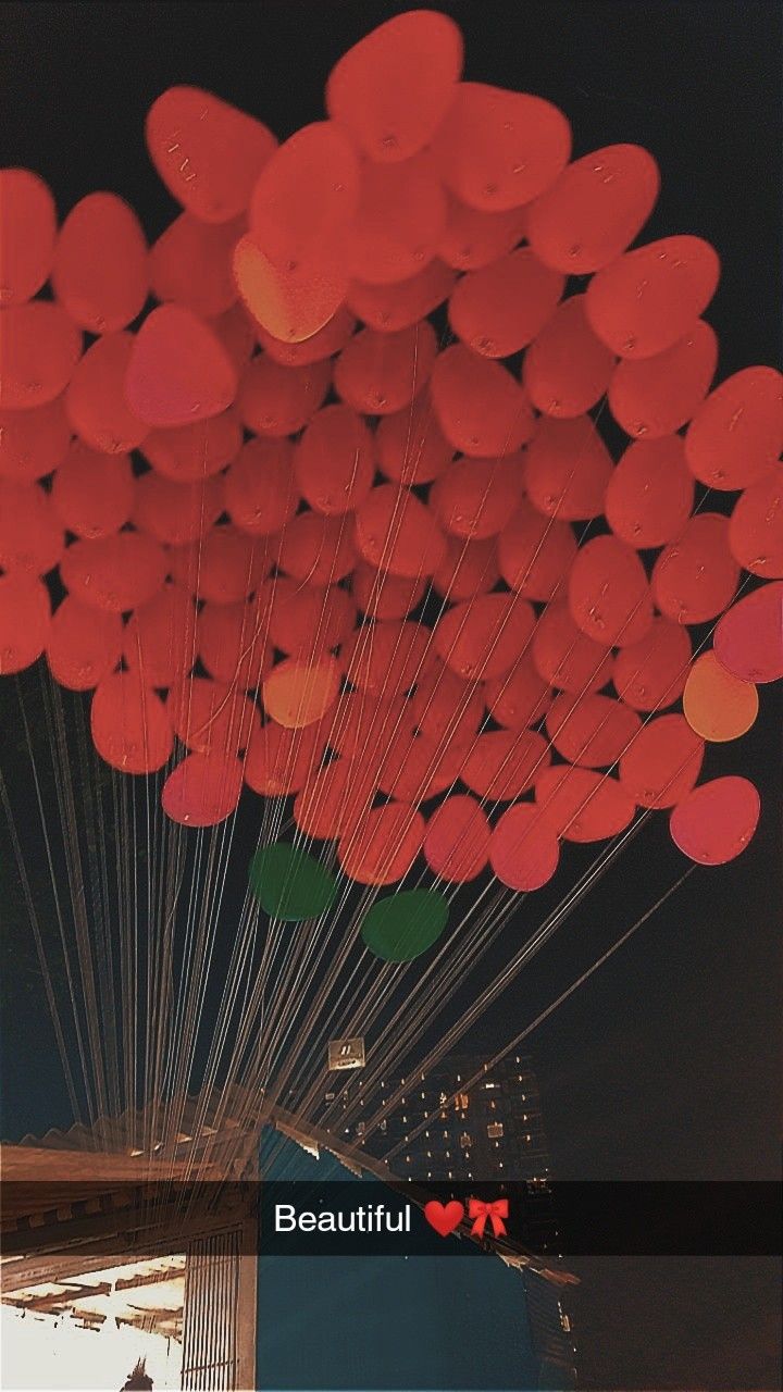 a bunch of red balloons floating in the air over a body of water at night