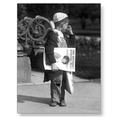 a little boy standing on the sidewalk talking on a cell phone and holding a sign