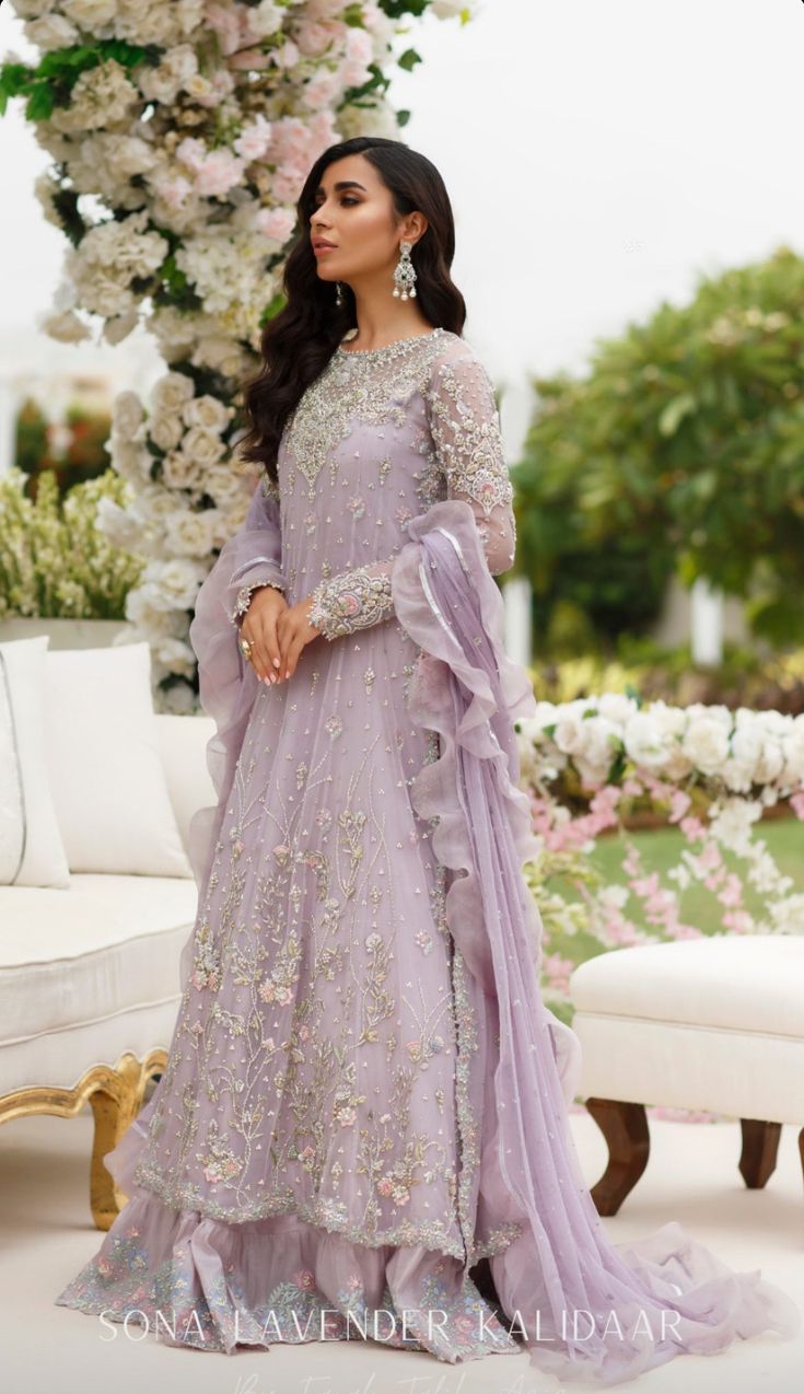 a woman in a lavender colored gown standing near a floral arch with flowers on it