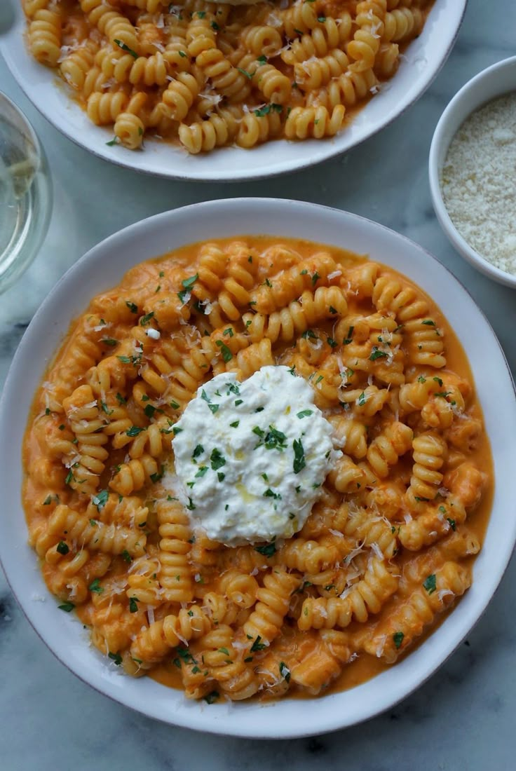 two white plates filled with pasta and sauce on top of a marble table next to silverware