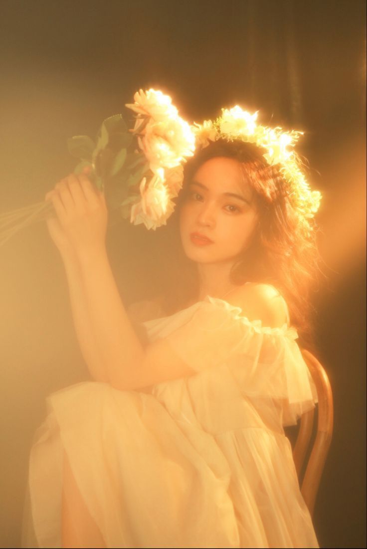 a woman sitting in a chair with flowers on her head and hands behind her back