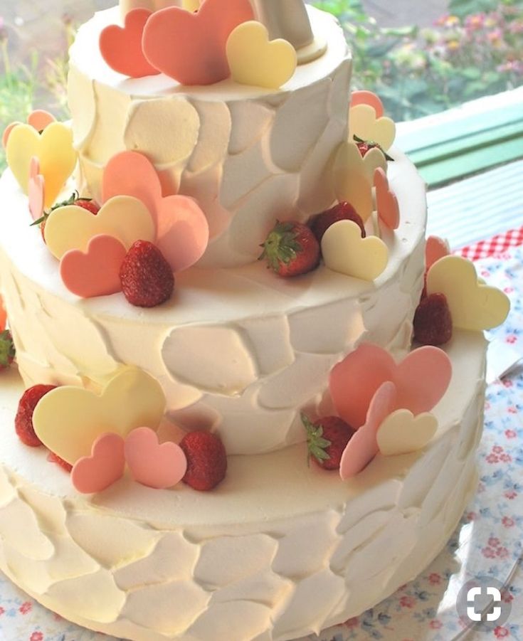 a three tiered cake with hearts and strawberries on the top is ready to be eaten