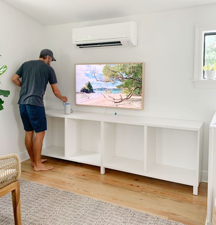 a man standing in front of a flat screen tv mounted on a wall next to a wooden floor