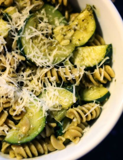 a white bowl filled with pasta and cucumbers covered in parmesan cheese