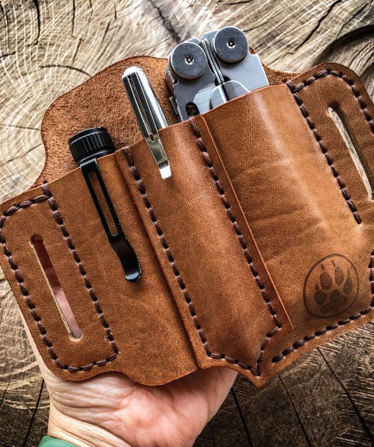 a hand holding a brown leather case with two pens and an electronic device in it