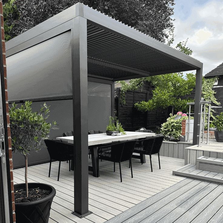 an outdoor dining area with table and chairs on wooden decking next to potted plants