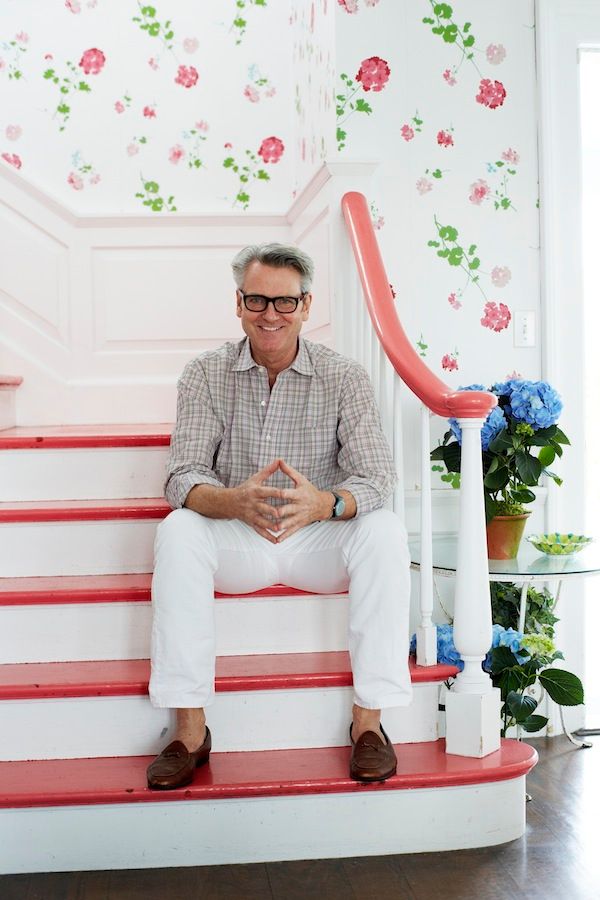 a man sitting on top of a red and white stair case next to a flowered wall