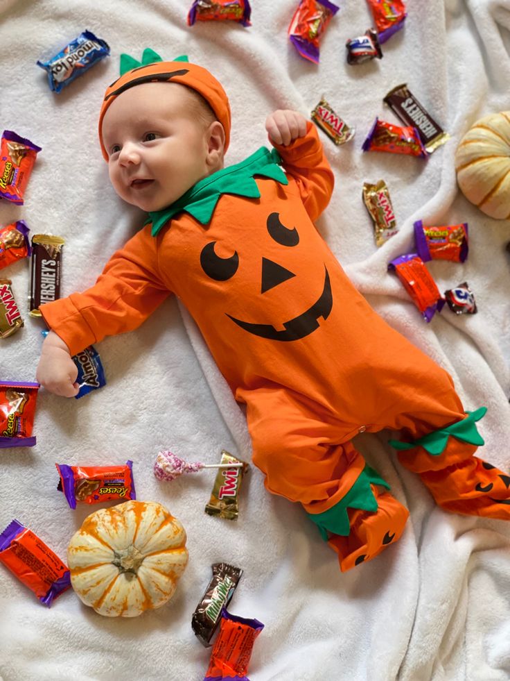 a baby dressed as a pumpkin laying on top of a blanket next to candy bars