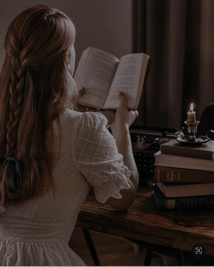 a woman sitting at a desk with an open book in front of her, reading