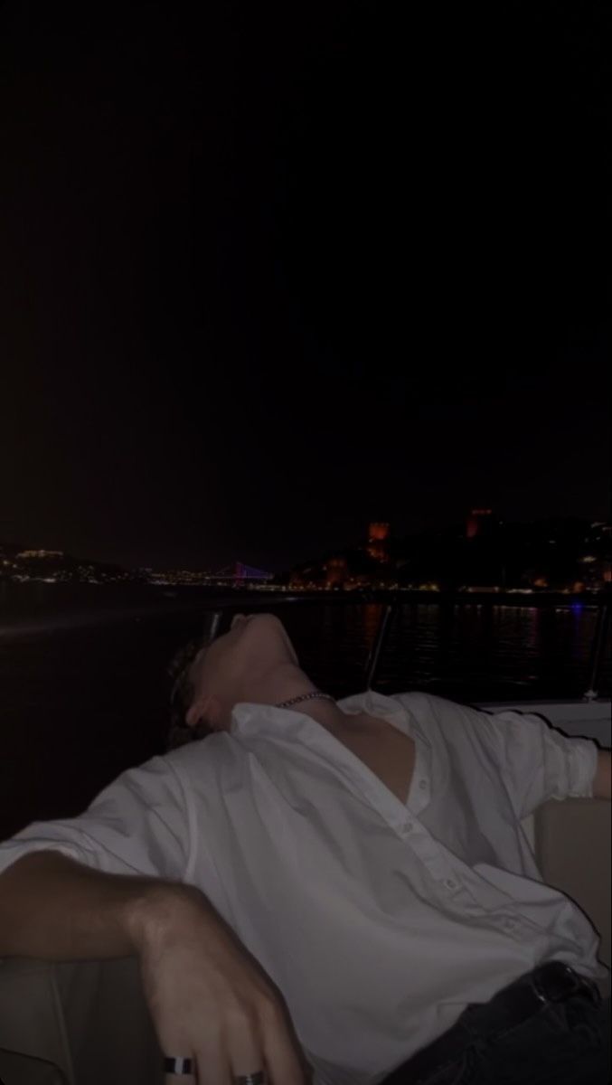 a man laying on the back of a boat in the water at night with his eyes closed