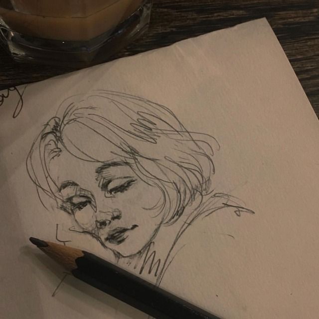 a pencil drawing of a woman's face on paper next to a cup of coffee