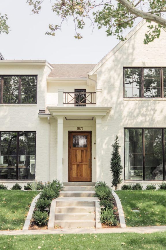 a large white house with black windows and steps leading up to the front door that is flanked by green grass