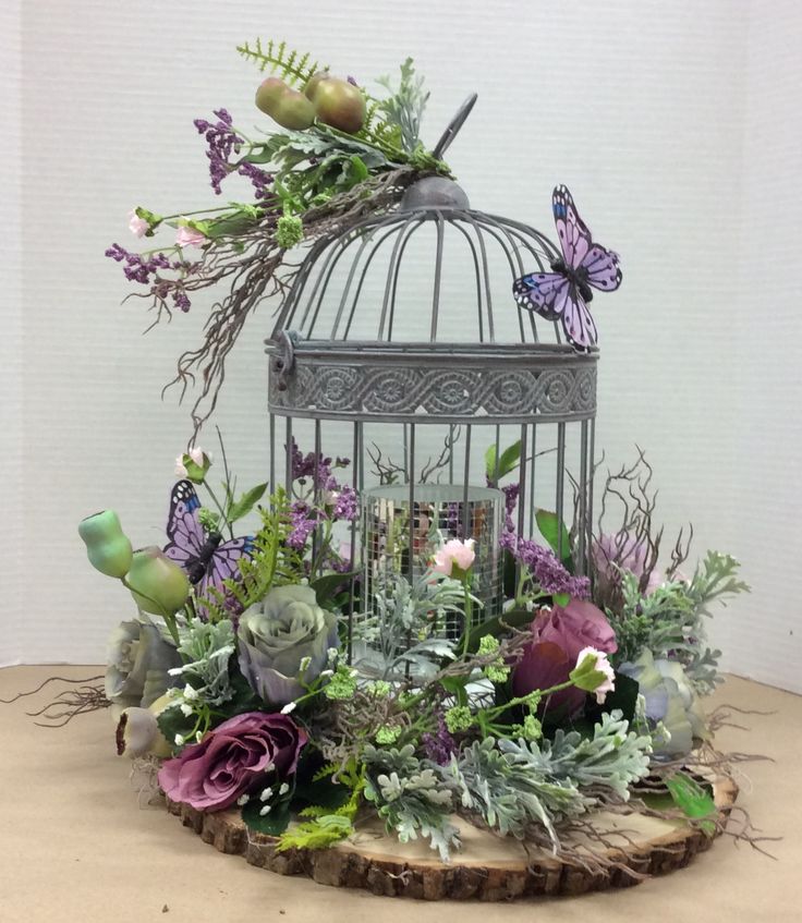 a birdcage filled with lots of flowers and greenery next to a butterfly