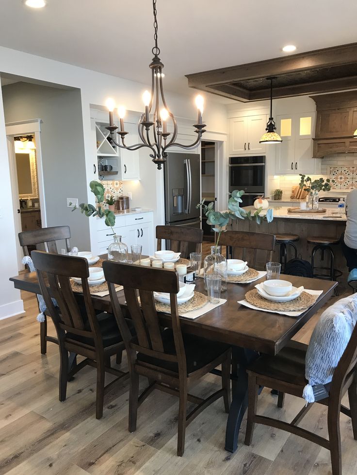 a dining room table set with place settings and plates on it, in front of the kitchen island