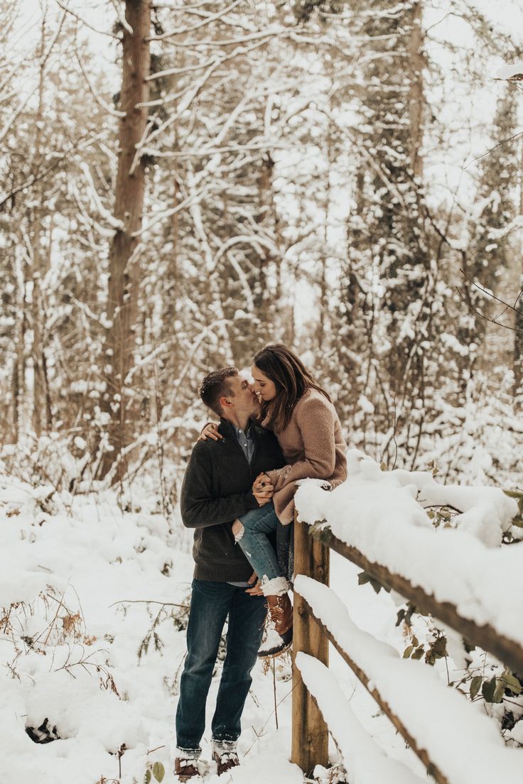 a man and woman kissing in the snow by a fence with lots of snow on it