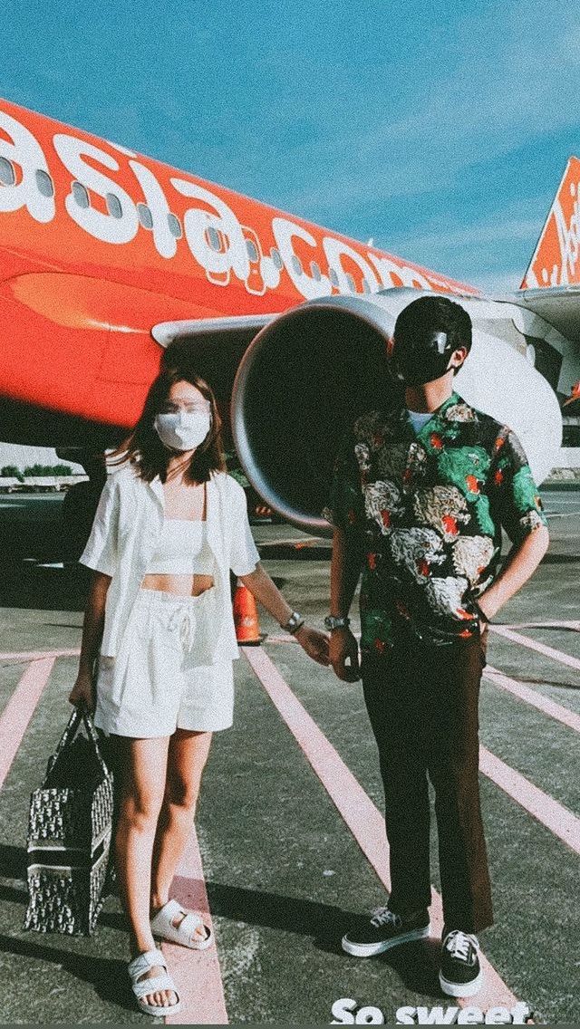 a man and woman standing in front of an airplane on the tarmac holding hands