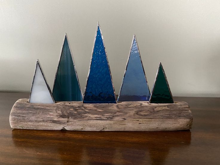 a group of blue and green glass trees sitting on top of a wooden table next to a white wall