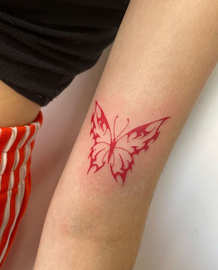 a woman's arm with a red butterfly tattoo on the left side of her leg