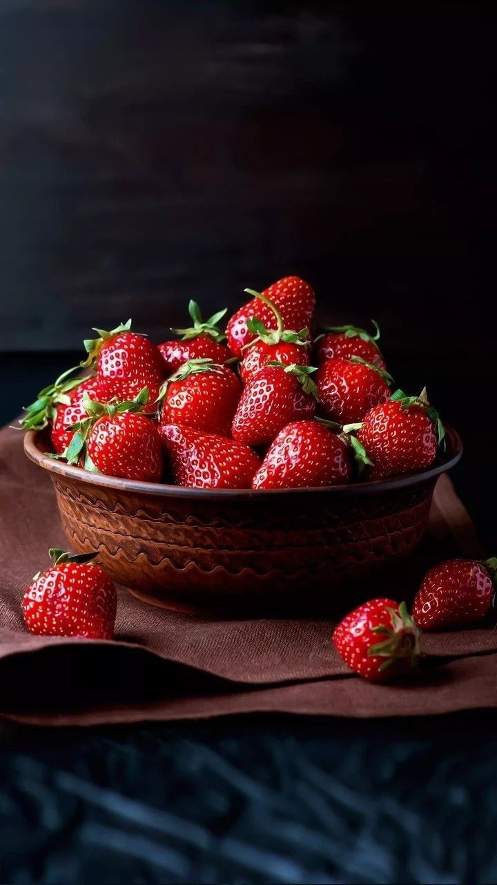 a bowl filled with lots of ripe strawberries on top of a brown table cloth