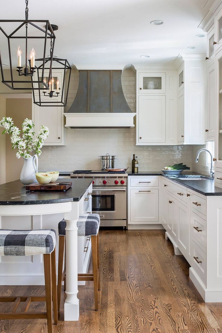 a kitchen with white cabinets and black counter tops, an island in the middle is surrounded by stools