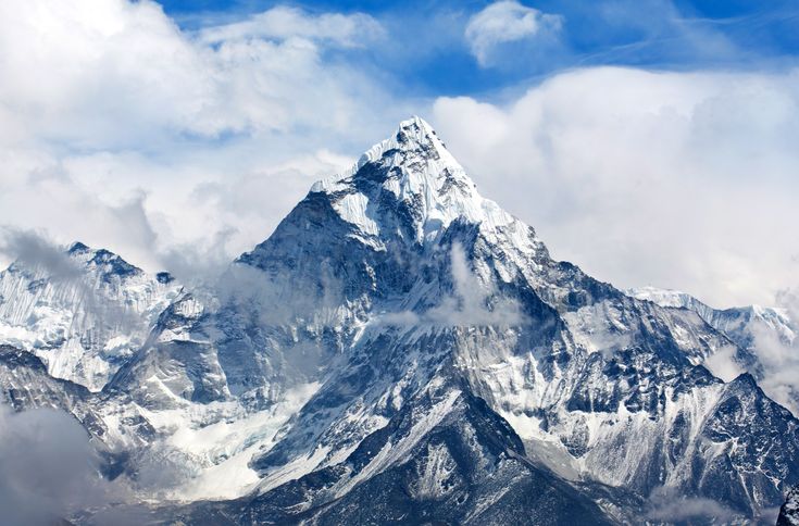 the top of a snow covered mountain with clouds in the foreground