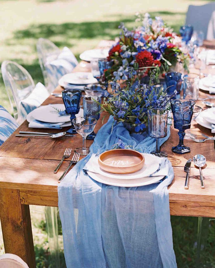 a wooden table topped with plates and vases covered in blue cloth draped over it