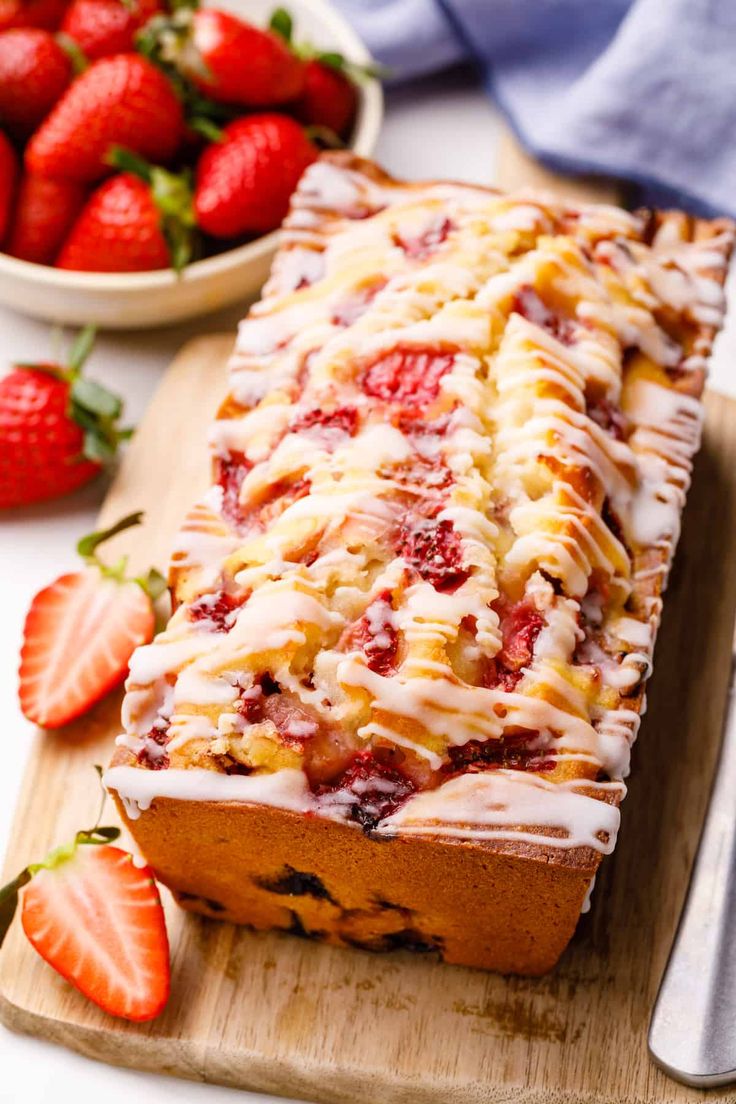 a loaf of strawberry bread sitting on top of a cutting board next to strawberries