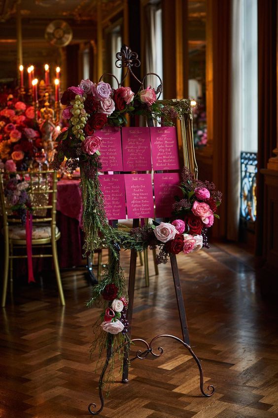 a pink sign with flowers and greenery on it sitting in front of a table