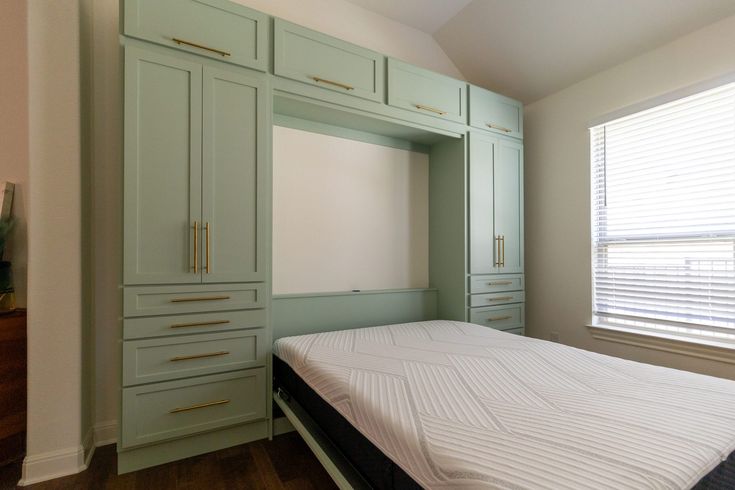 an empty bedroom with green cabinets and a white bed in it's center area