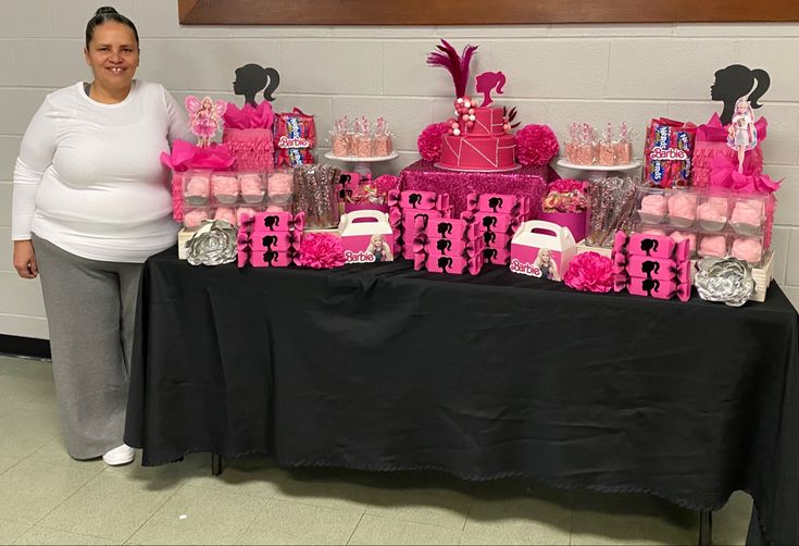 a woman standing next to a table covered in pink and black cakes, cupcakes and candies