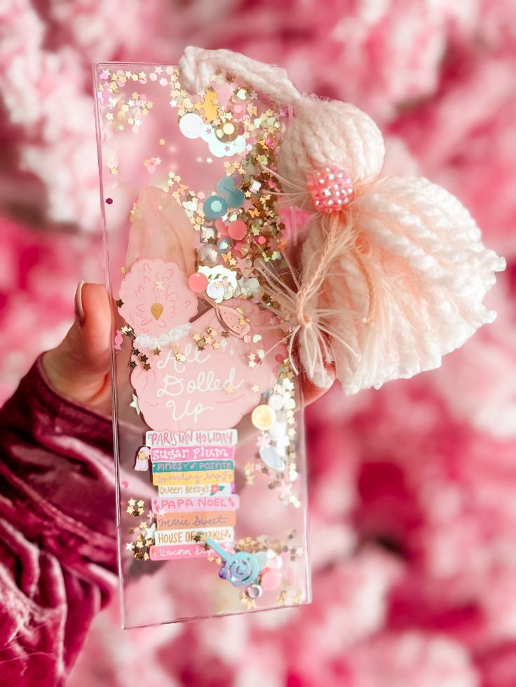 a person holding up a clear case with pink flowers and pearls on the side,