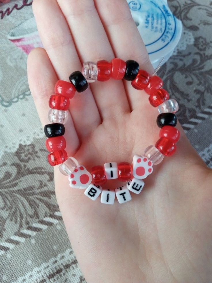 a hand holding a red and black beaded bracelet with words written on the beads