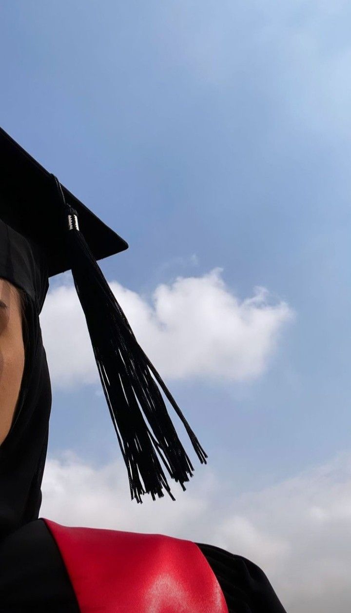 a woman wearing a graduation cap and gown in front of a blue sky with clouds