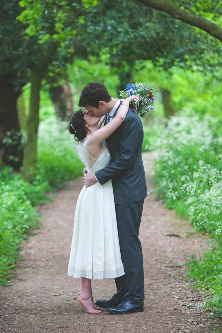 a bride and groom kissing on a dirt path in the middle of a wooded area