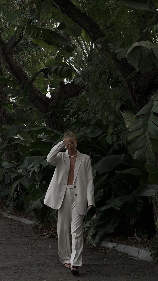 a woman is walking down the street talking on her cell phone while wearing a white suit