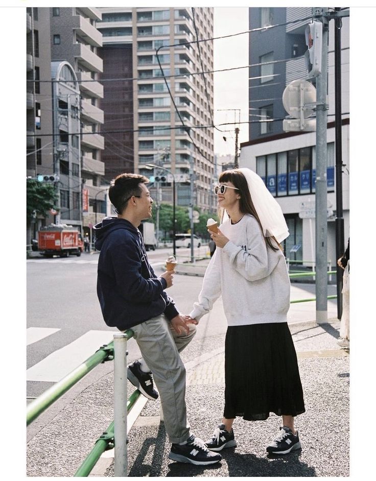 a man and woman standing next to each other on a street corner eating ice cream