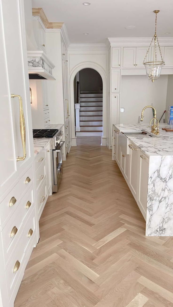 a large kitchen with white cabinets and marble counter tops, along with herringbone wood flooring