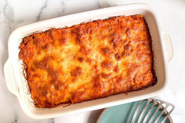 a casserole dish with cheese and meat in it on a marble counter top