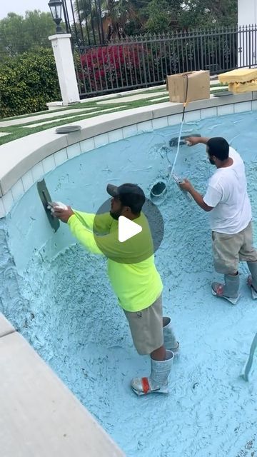 two men in yellow shirts are painting a pool