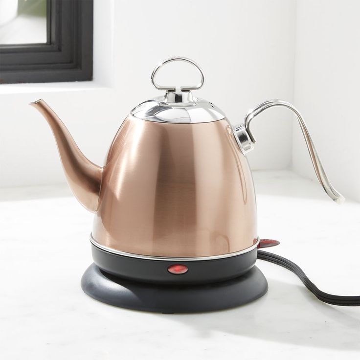 a metallic tea kettle sitting on top of a white counter next to a window with a black handle