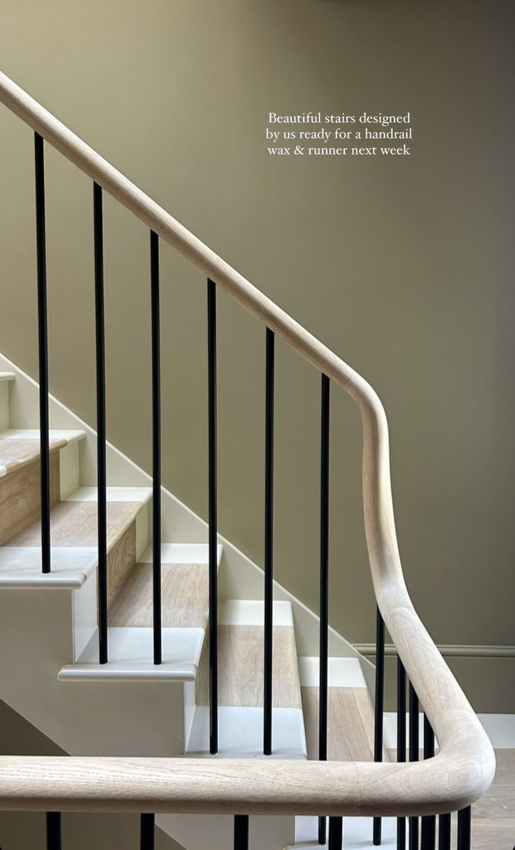 a white staircase with black handrails next to a beige wall and wooden floor