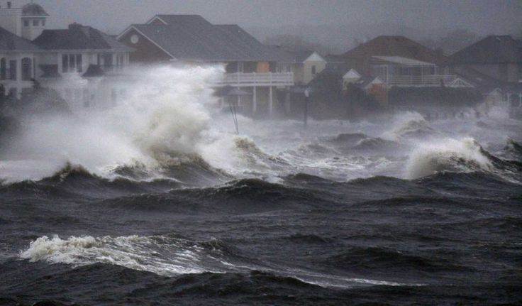 a large wave is crashing over houses in the middle of the ocean with homes in the background